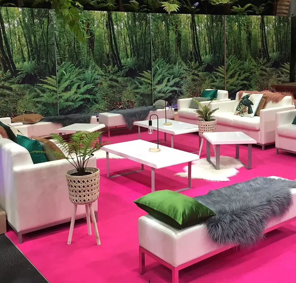Peek Exhibition Lounge set up, images of forest printed on wall panels, bright pink carpet with white furniture and colorful throws